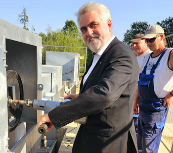 Umweltminister Prof. Dr. Armin Willingmann nimmt das Absperrbauwerk in Betrieb. Er steht an der Vorrichtung, mit der das Werk geschlossen und geöffnet werden kann. Er blickt in die Kamera und lächelt. 