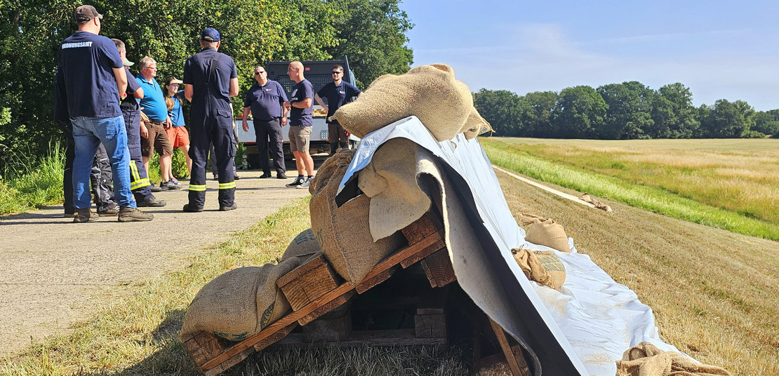 Foto von einer Wasserwehrschulung: Im Vordergrund eine Deicherhöhung mit Europaletten und Planen, im Hintergrund Schulungsteilnehmer