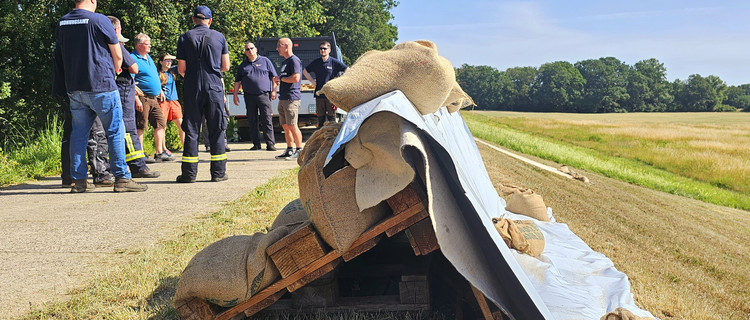 Foto von einer Wasserwehrschulung: Im Vordergrund eine Deicherhöhung mit Europaletten und Planen, im Hintergrund Schulungsteilnehmer
